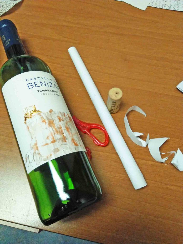 A paper rolled on the table beside a cork cap, scissors, and a green wine glass.