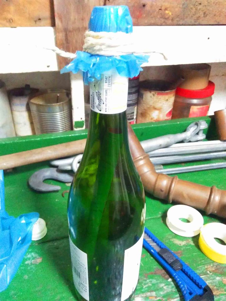 A green bottle with a letter inside it placed surrounded by various tools all on the green table.