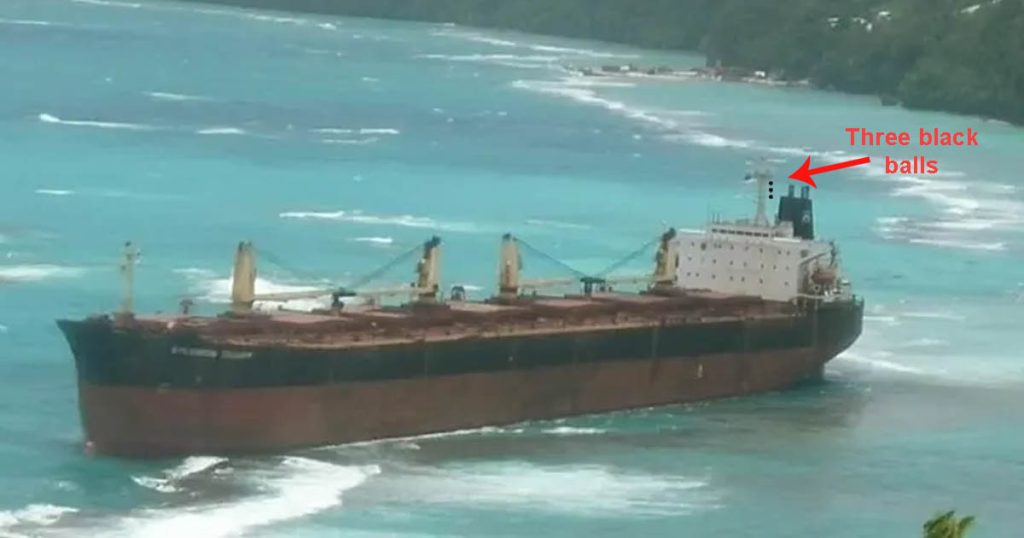 A huge bulk carrier aground near the shore. You can see three black balls on her mast.
