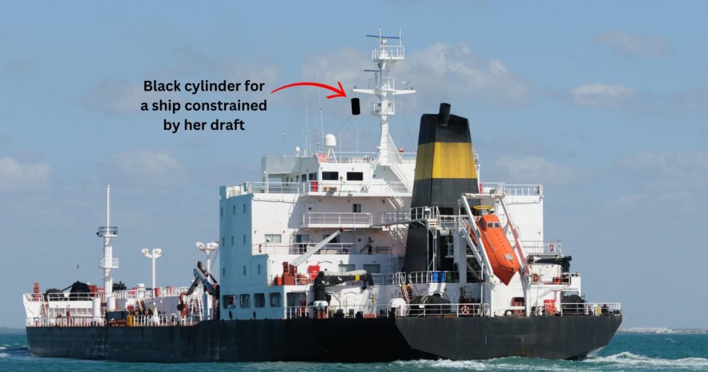 A ship showing a black cylinder day shape on her mast indicating she is constrained by her draft.