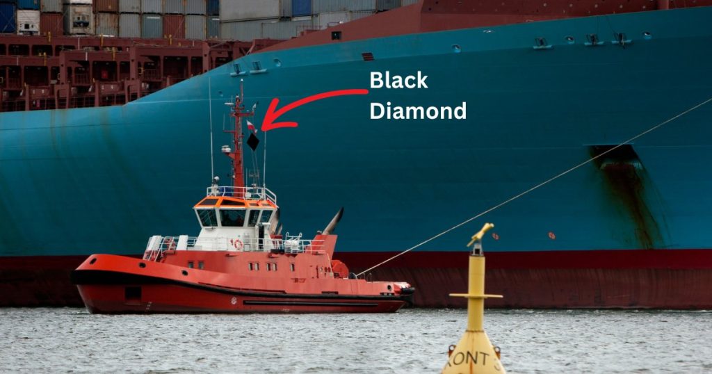An orange tugboat showing a diamond shape on its mast while towing a huge vessel with a blue hull.