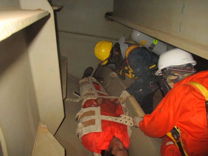Two deck crew wearing a breathing apparatus rescuing another crew and strapping him into a stretcher during an enclosed space rescue drill.