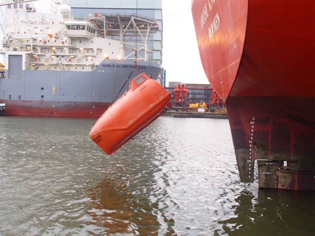 An orange fully enclosed free-fall lifeboat lowered on the water.