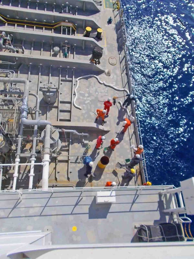 Ship's crew on deck performing an oil sprill drill using, shovels. sorbent booms, sawdusts, and dust pans to collect the spills.